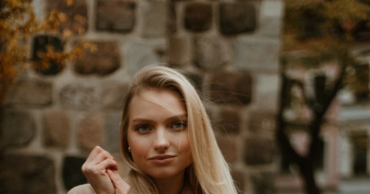 Balayage blonde beige - ung kvinne med langt lyst hår og beige genser foran steinbyggning.