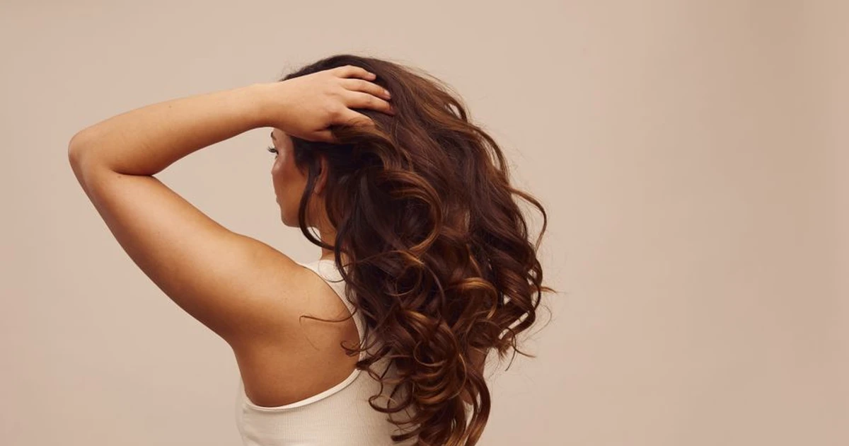 Balayage brunt hår på kvinne sett bakfra med hånd i håret mot beige bakgrunn.