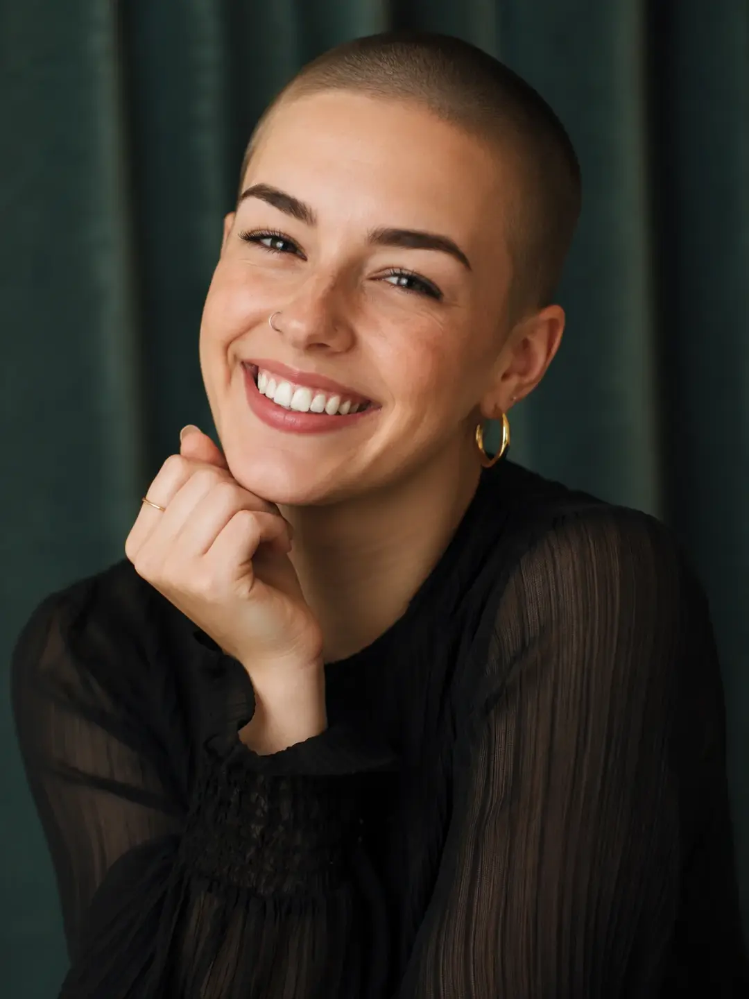 Kvinne med buzz cut, kort frisyre som uttrykker selvtillit og stil med sort skjorte mot grønn bakgrunn.